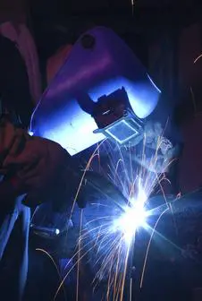 Welder uses torch to make sparks during manufacture of metal tube.